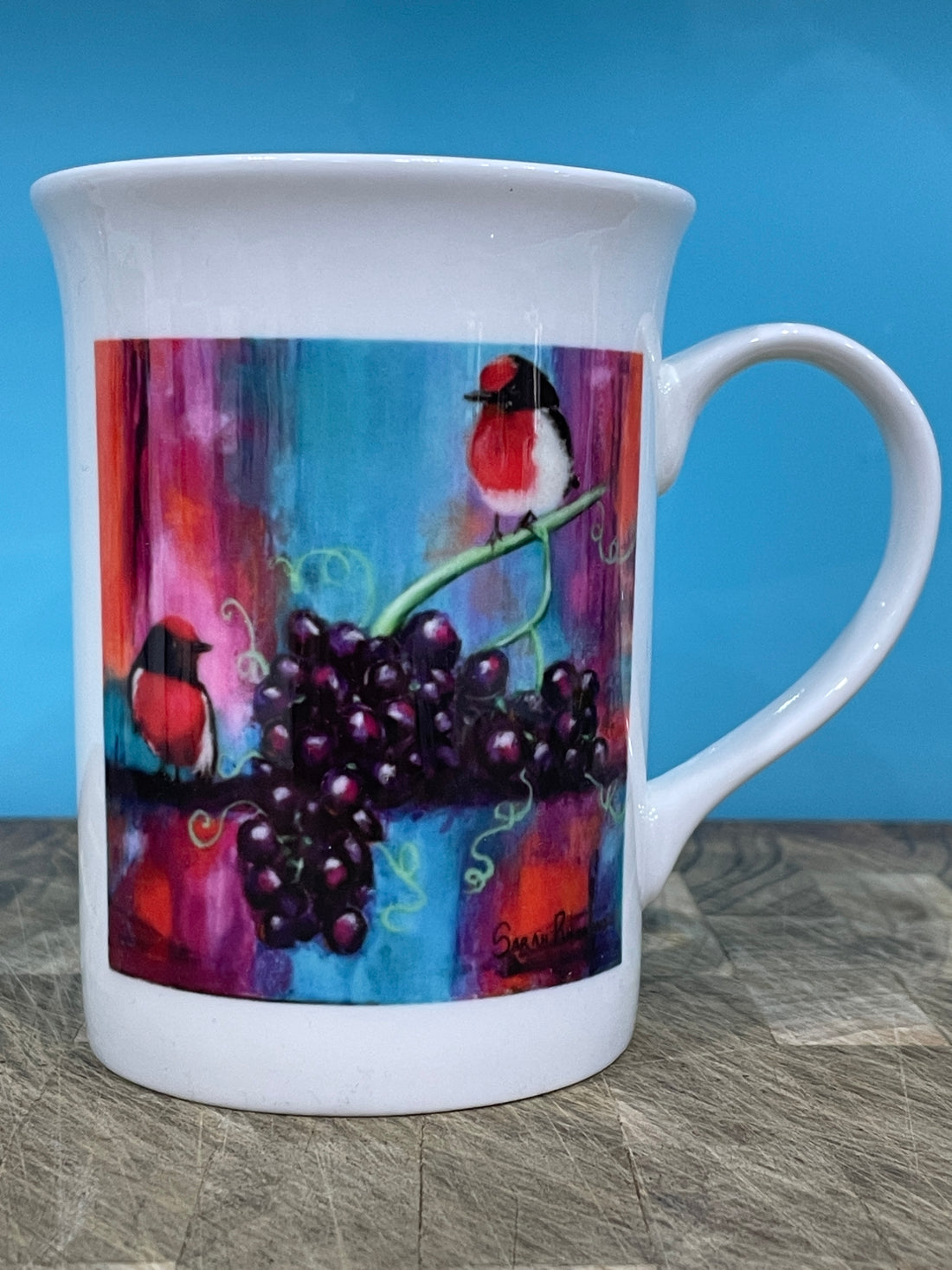 White bone china coffee mug with print of abstract realism red robins with red grapes on colourful abstract background.